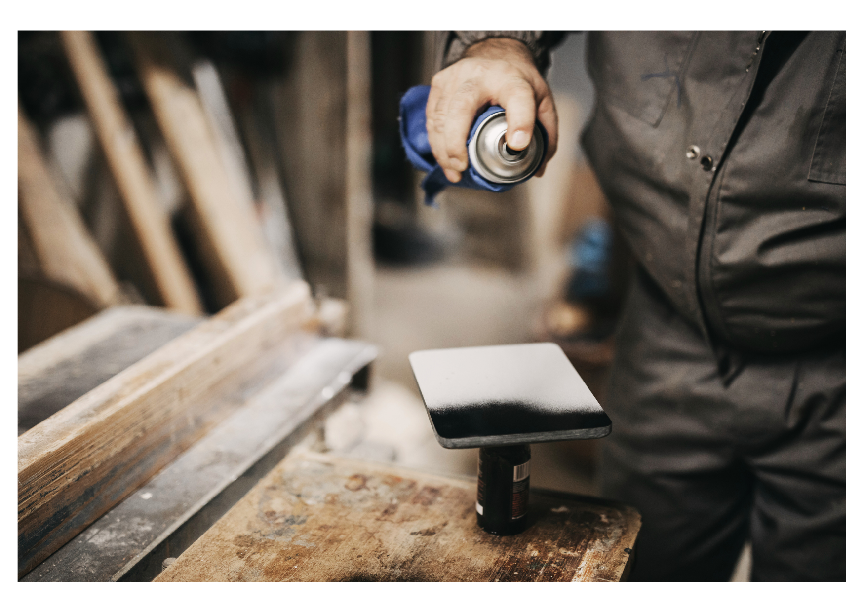 Artisan utilisant une bombe de peinture pour recouvrir de manière homogène une plaque de bois dans un atelier.