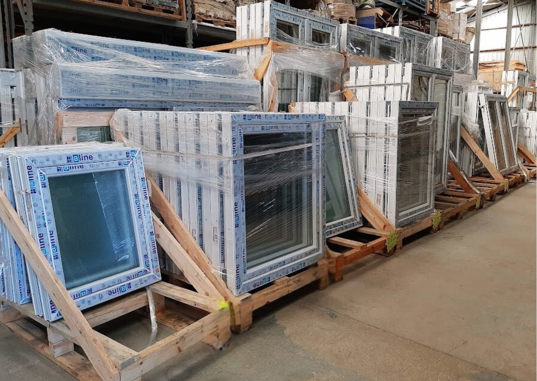Palette de châssis abattants en PVC blanc stockés dans l'entrepôt du Marais Fleuri.