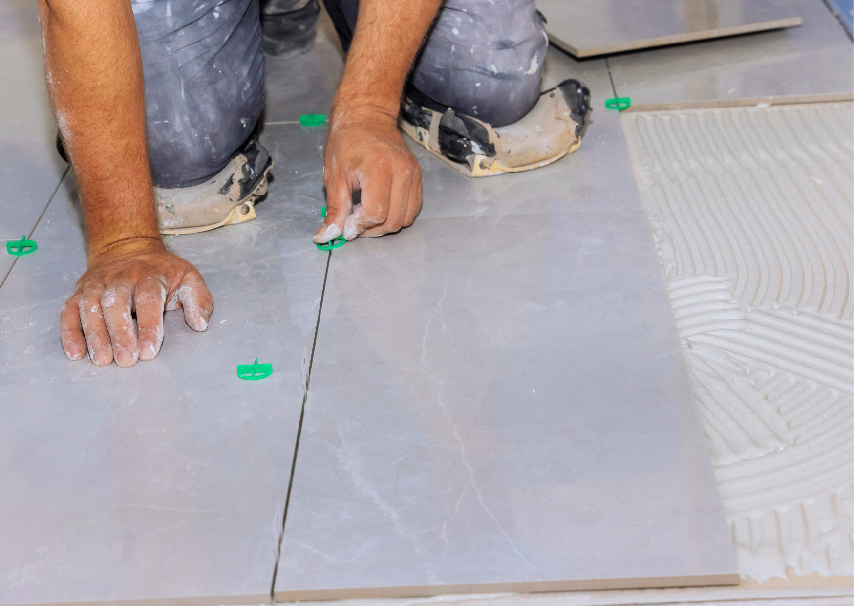 Artisan carreleur plaçant des croisillons en plastique vert pour garantir l'alignement et la régularité des joints de carrelage au sol.
