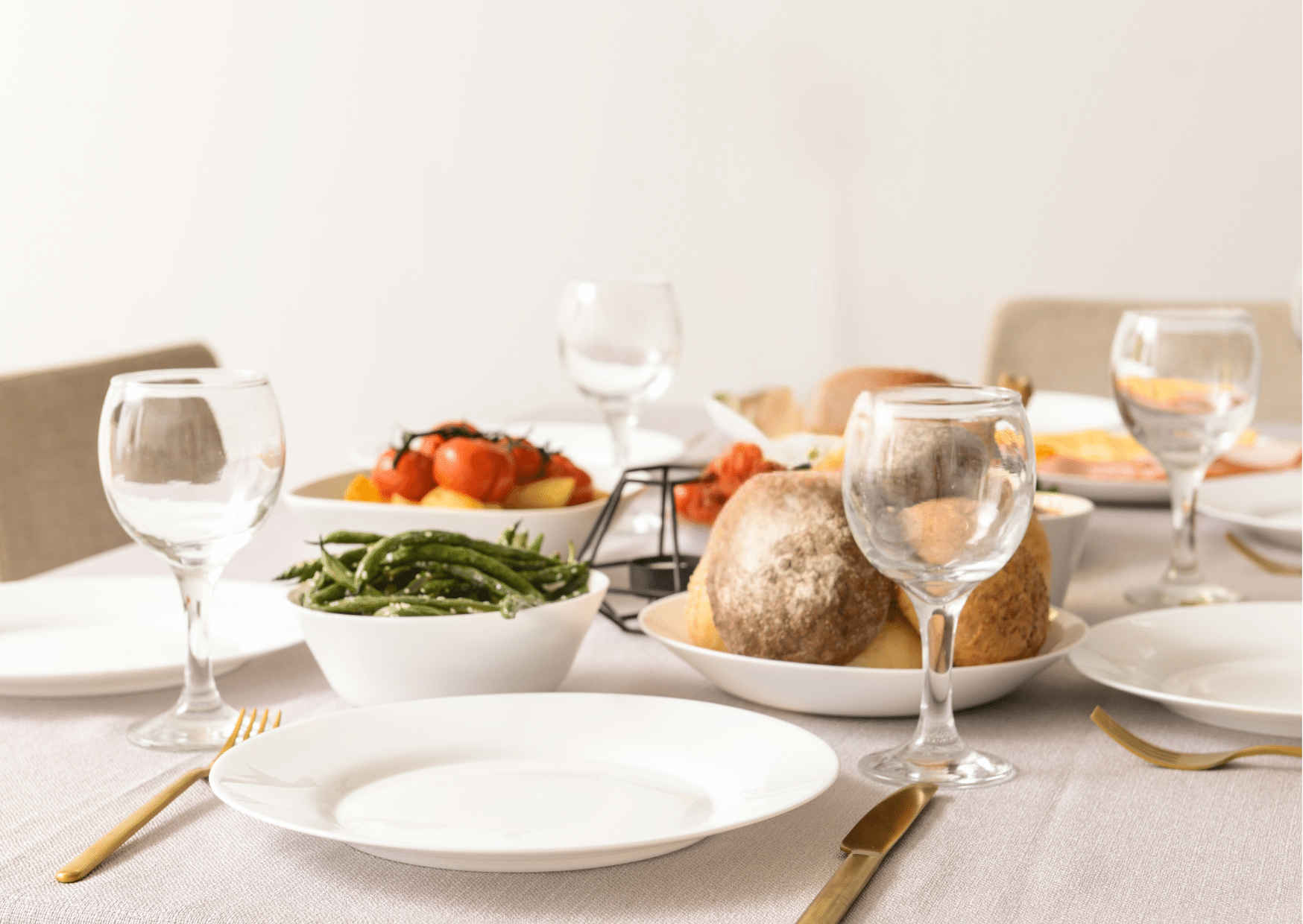 Mise en scène d'une table en bois clair avec vaisselle blanche et plats de légumes, style minimaliste et naturel.