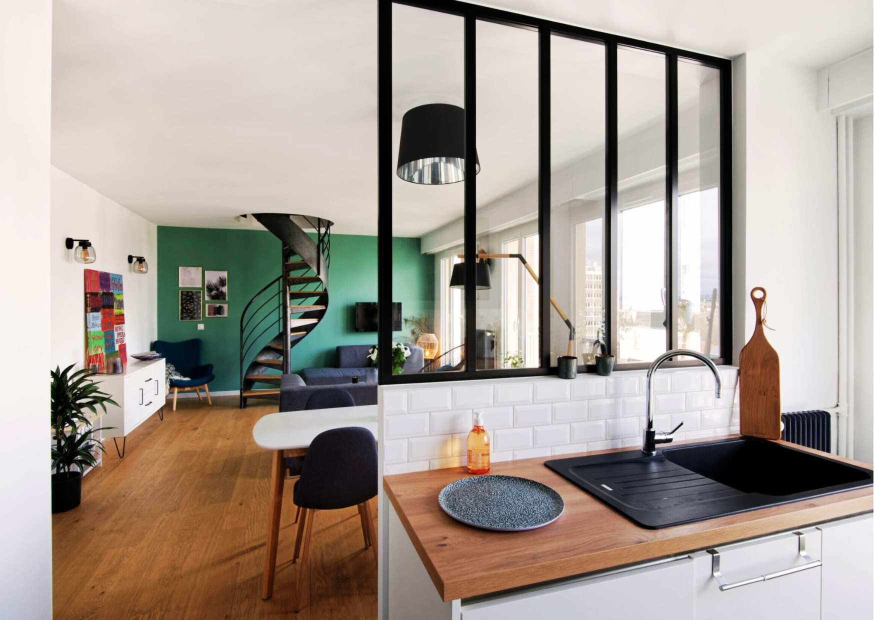 Verrière à montants noirs posée sur un muret de cuisine blanche pour séparer l'espace repas du salon.