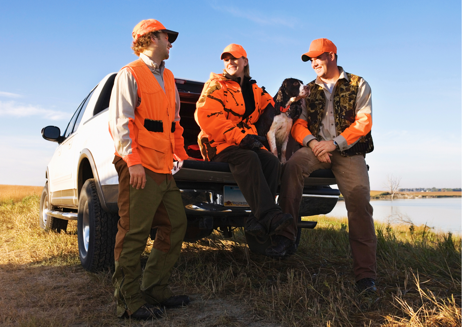 Groupe de chasseurs portant des gilets et casquettes orange de sécurité ainsi que des vêtements de camouflage à côté d'un véhicule tout terrain.