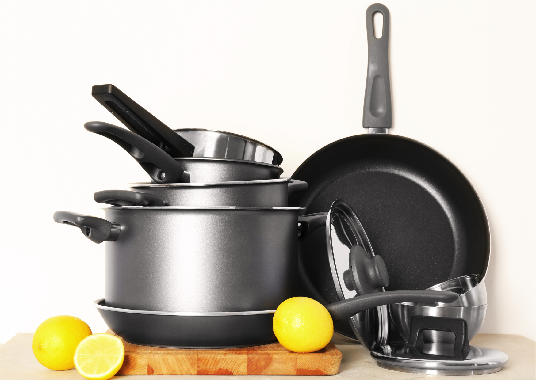 Ensemble de casseroles et poêles grises posées sur un plan de travail en bois massif avec des citrons frais.