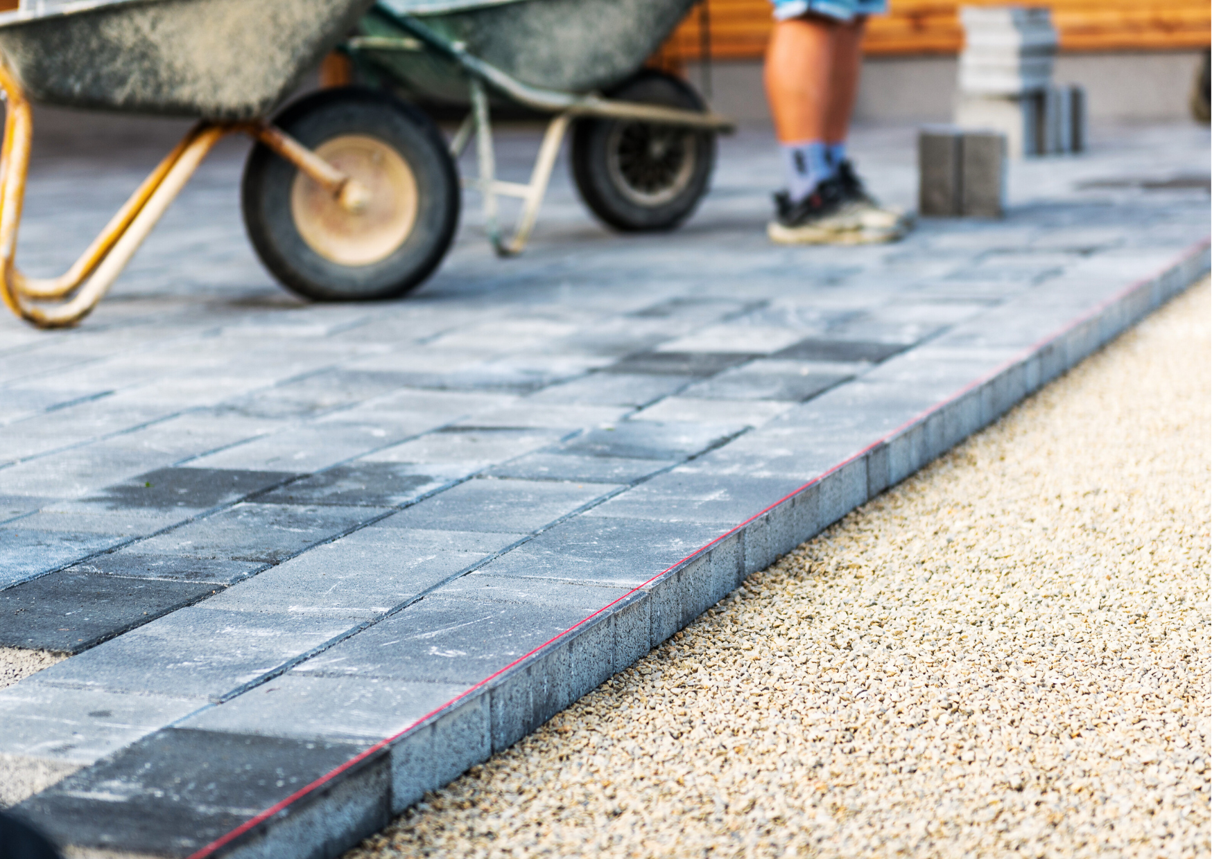 Installation de pavés gris sur lit de gravier avec alignement au cordeau rouge pour une terrasse parfaite.