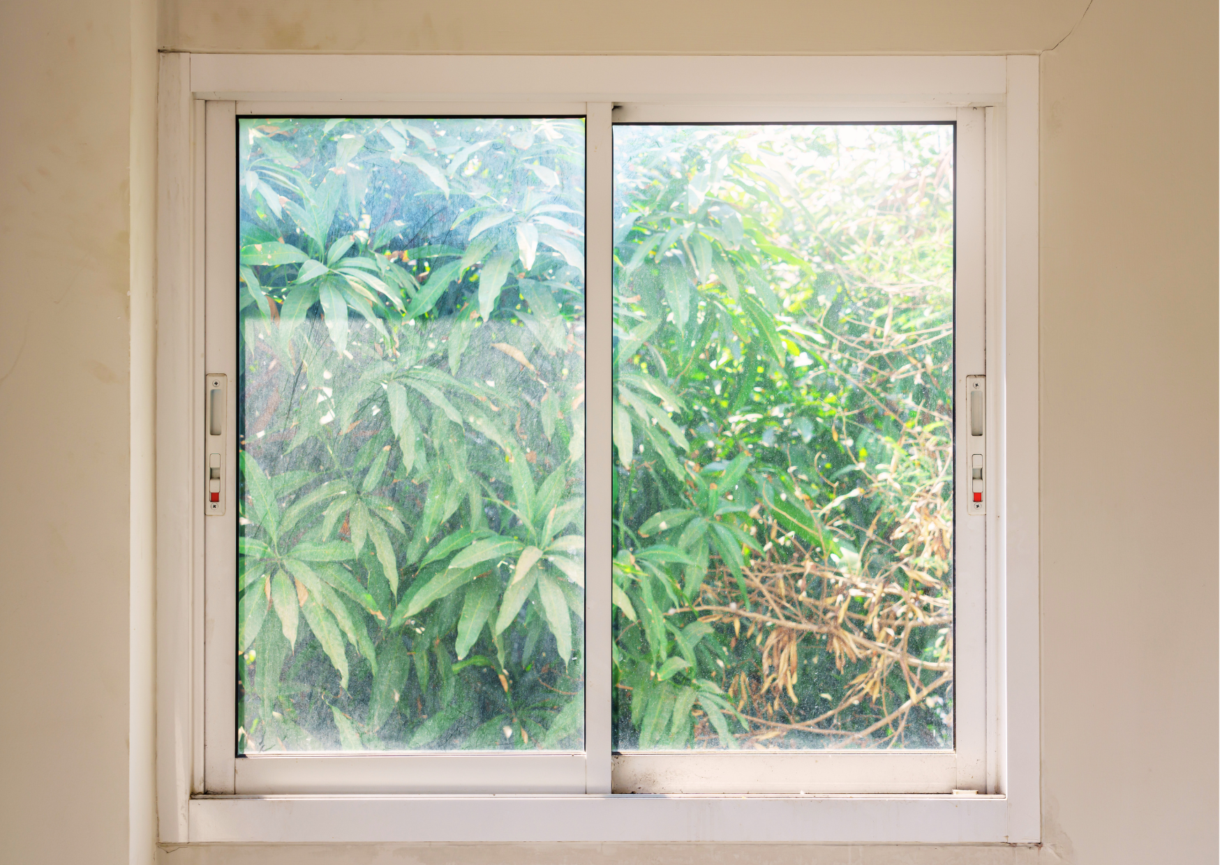 Fenêtre coulissante deux vantaux en PVC blanc posée en intérieur avec vue sur le jardin, disponible chez Marais Fleuri.