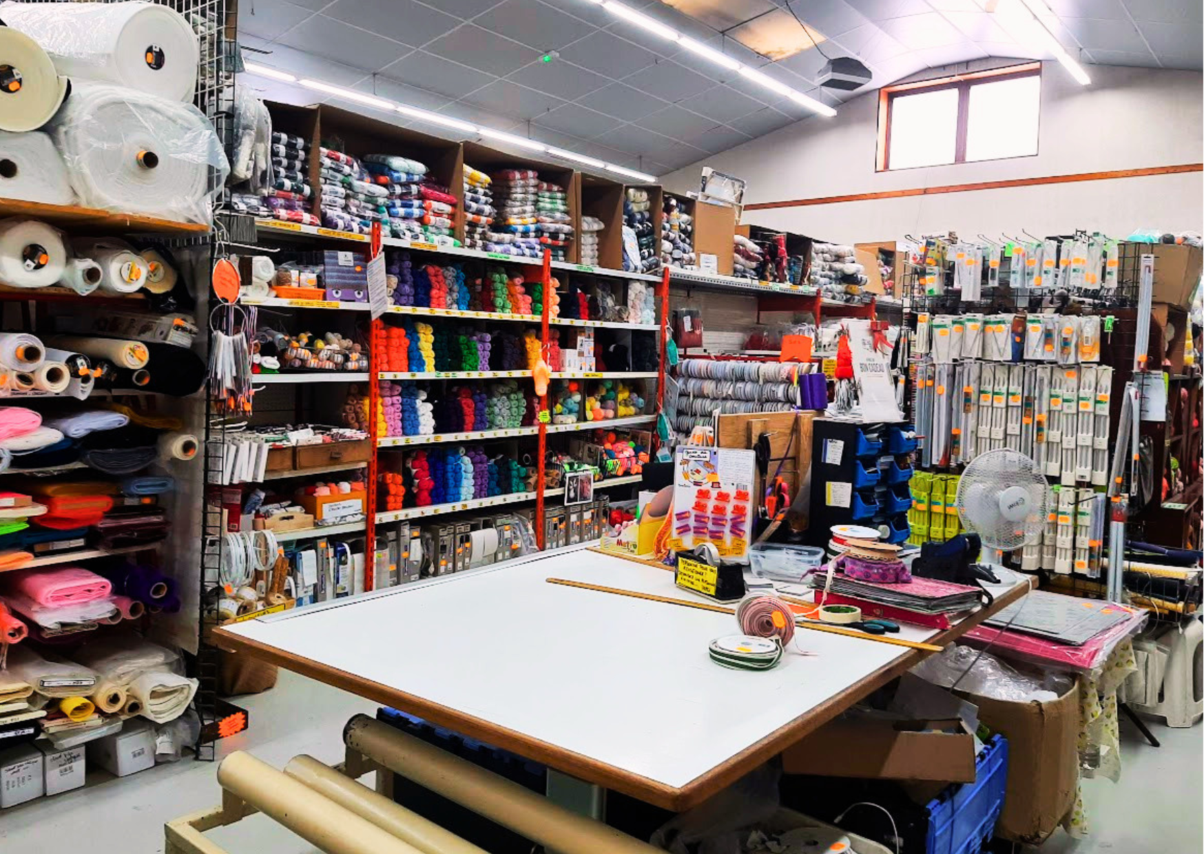 Espace mercerie avec un grand choix de pelotes de laine colorées, rouleaux de tissus et table de découpe chez Le Marais Fleuri à Marans (17) et Mareuil-sur-Lay (85).