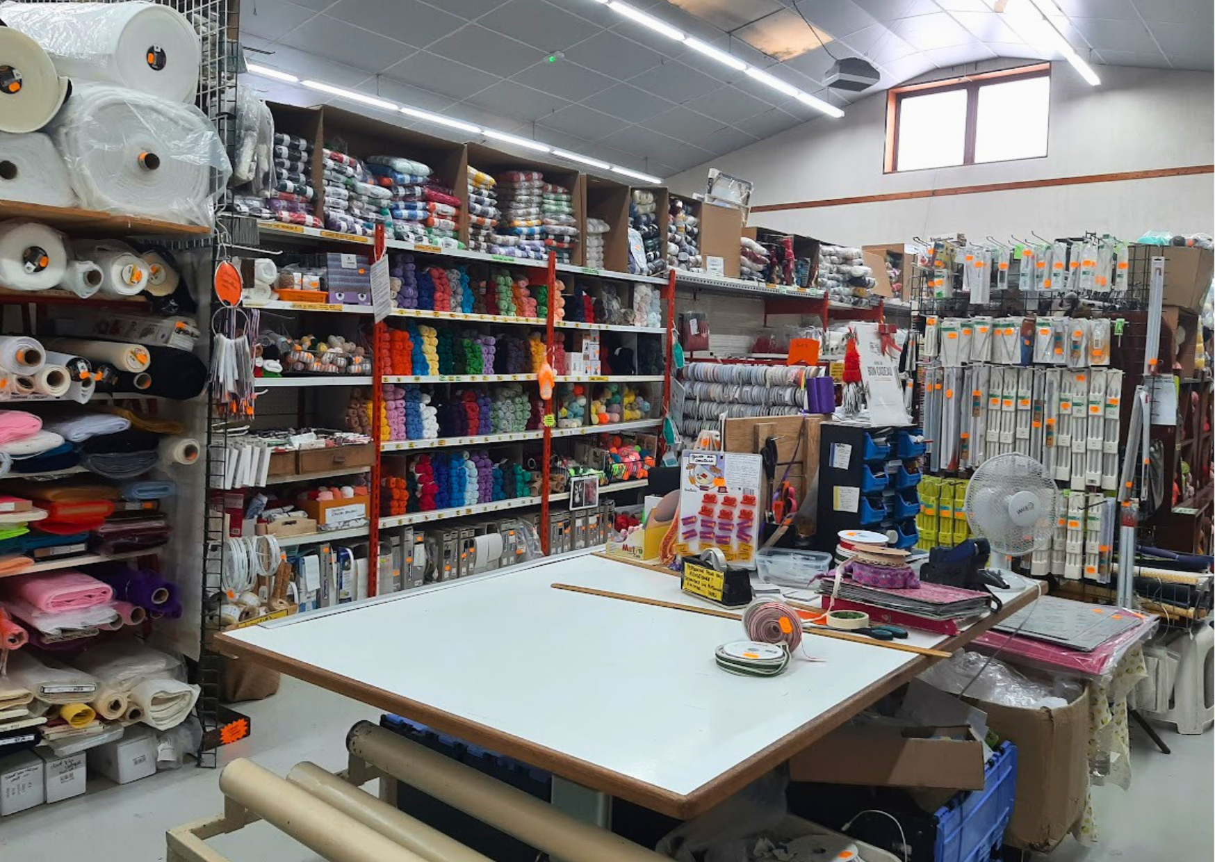 Rayon mercerie complet avec pelotes de laine, rouleaux de tissus, aiguilles et accessoires de couture en stock chez Marais Fleuri.
