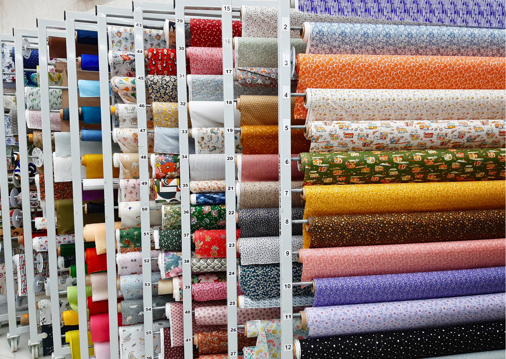 Présentoir de rouleaux de tissus imprimés et motifs colorés pour la couture au mètre chez Marais Fleuri.