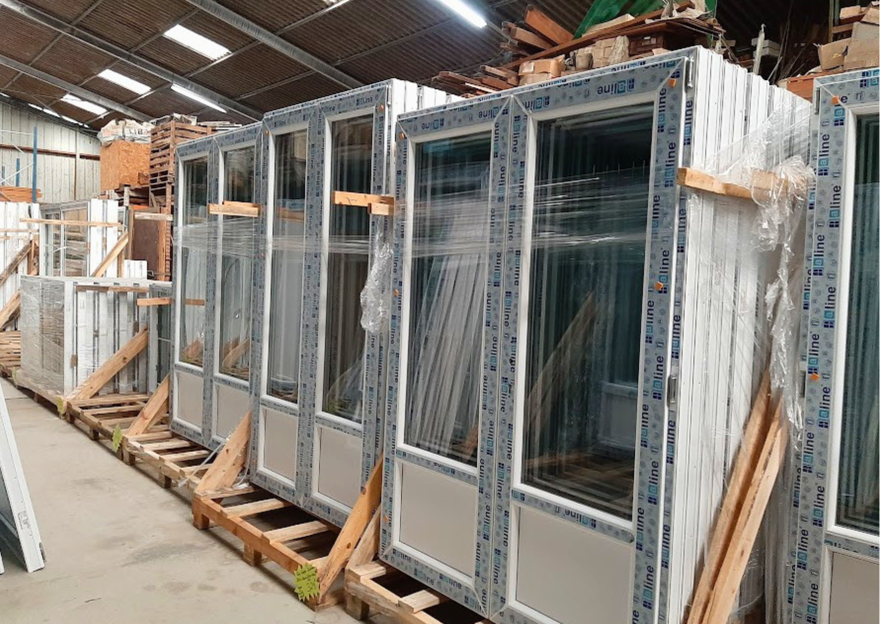Stock important de portes-fenêtres vitrées à 2 vantaux en PVC blanc neuves sur chevalets en bois dans le dépôt Marais Fleuri à Marans.