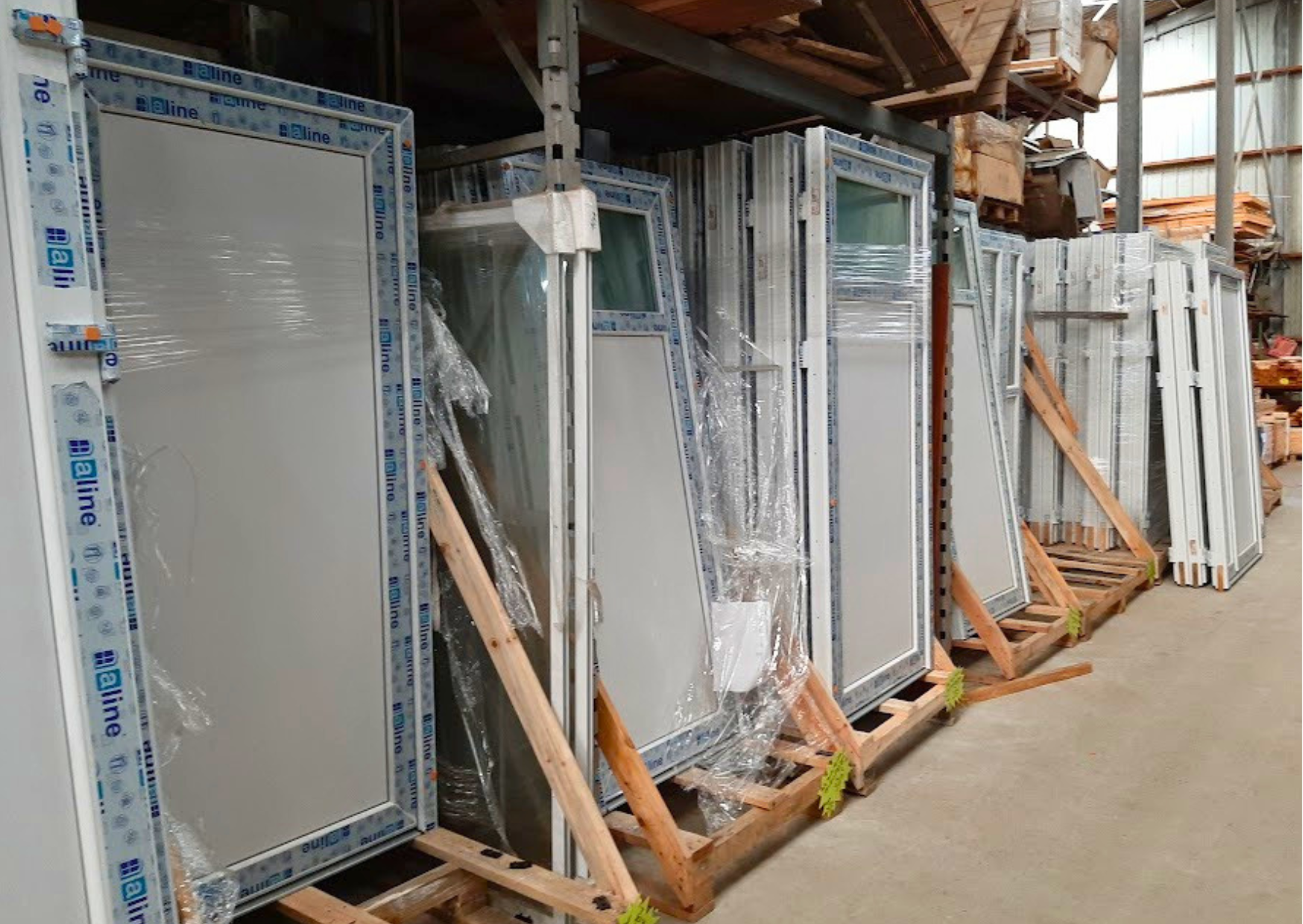 Stock de portes d'entrée et de portes de service en PVC blanc sur chevalets en bois chez Marais Fleuri à Marans (17) et Mareuil-sur-Lay (85).